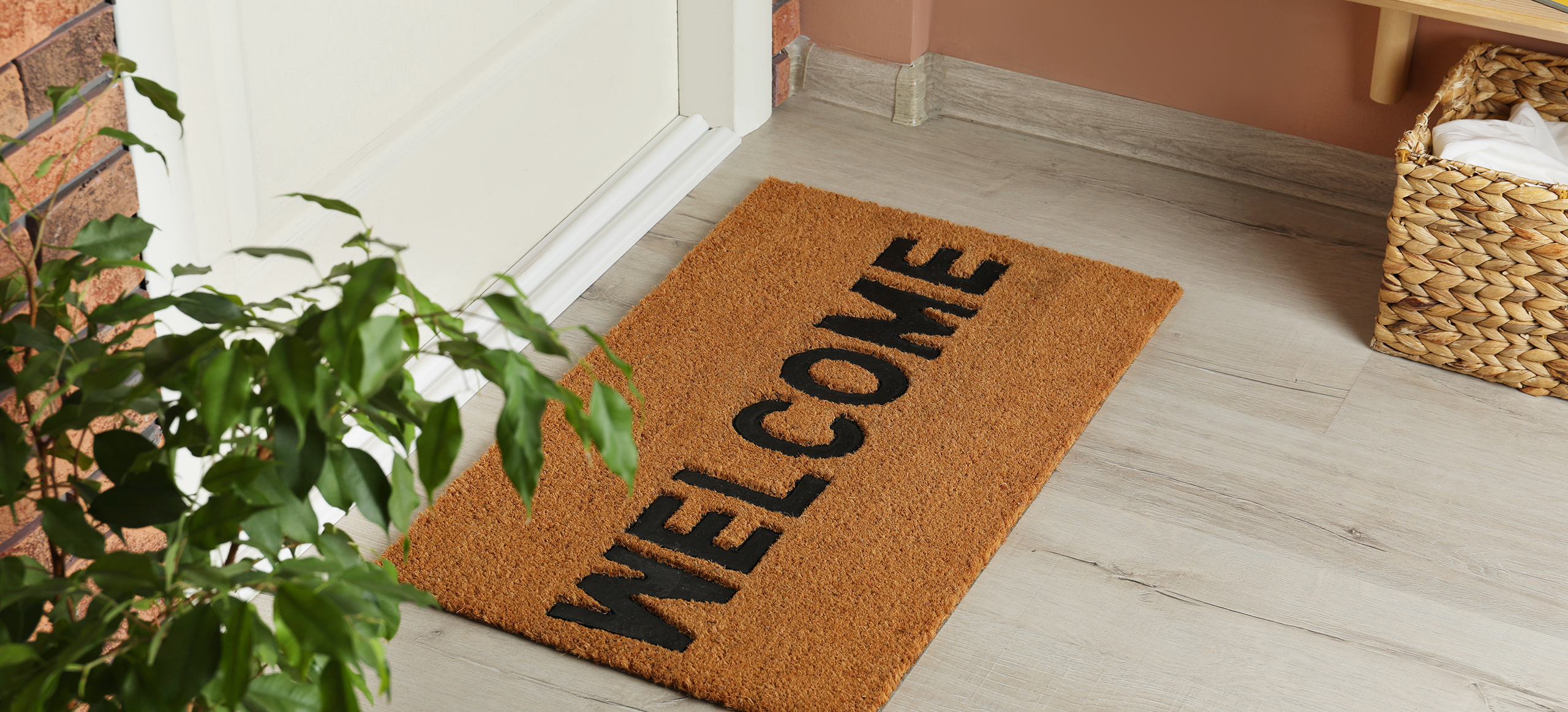 Door mat with word Welcome on wooden floor in hall